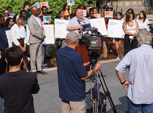 Bill Sinclair speaking during a press conference with youth standing behind him and people from the media in the foreground