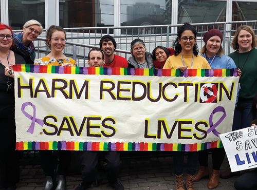 people standing with a sign that reads: Harm Reduction Saves Lives