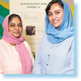 two women standing in front of a sign with the title "Muslim Women who Inspire us"