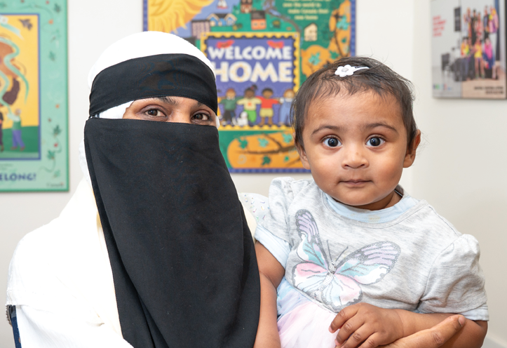 woman holding her toddler with a poster in the background with the title 
